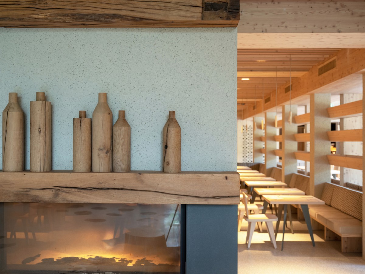hotel bohinj Sodobna, minimalistična notranjost restavracije z lesenim dekorjem v obliki steklenic na kaminu, lesenimi mizami in stoli ter svetlo leseno oblogo ustvarjajo toplo in vabljivo vzdušje.